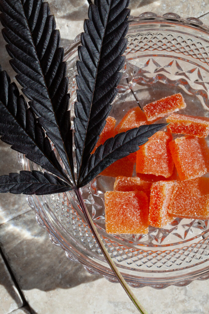 Cannabis-infused or CBD gummy candies in a glass dish with cannabis leaf
