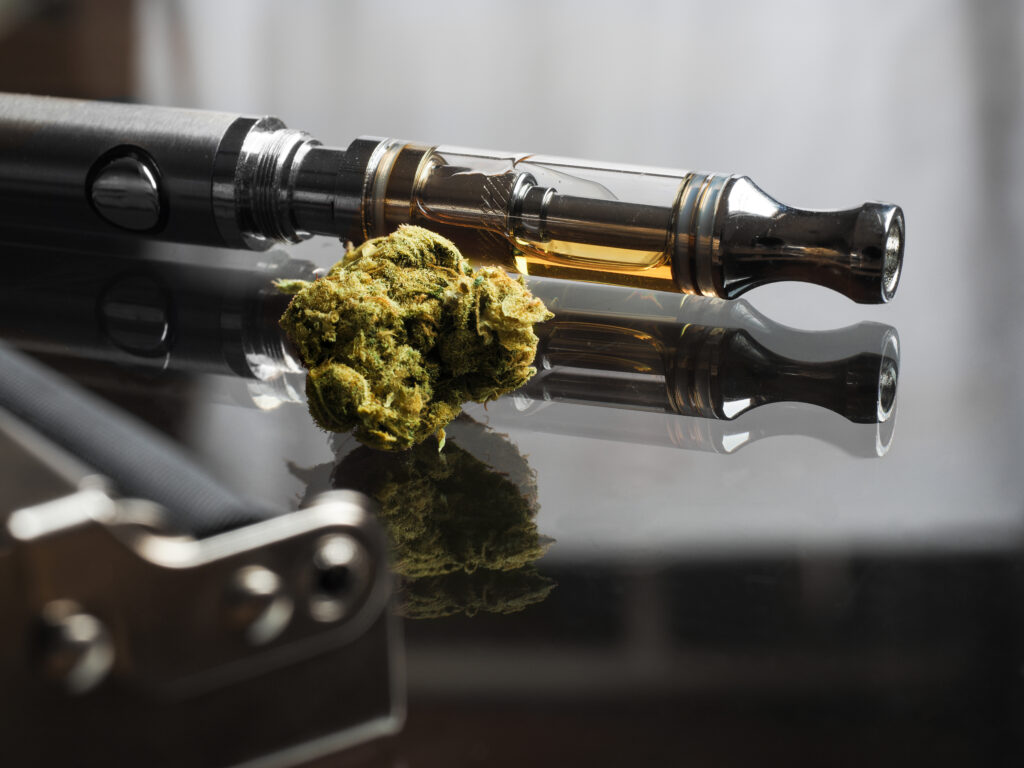 Close up shot of real cannabis or weed with cannabis oil in cartridge of vape pen in the background, roller blurred in foreground and text space on the right under the dark theme